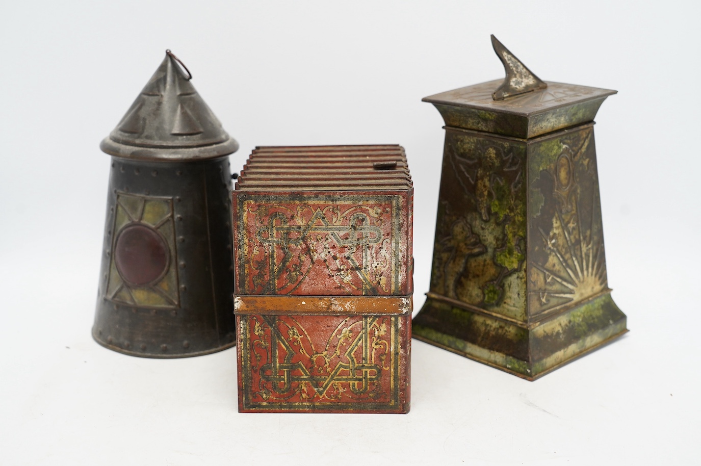 Three early 20th century Huntley & Palmer novelty biscuit tins, modelled as bound books, a sun dial and an Arts & Crafts lantern, largest 24cm high. Condition - fair